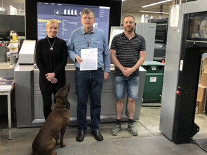 Sabine Krüger (Verantwortliche für die Vorstufe), Thomas Löhnert und Harald Weser (Drucker) (v. l. n. r.) freuen sich zusammen mit der "guten Seele" des Hauses, Firmenhund Gustav über die bestandene PSO-Zertifizierung